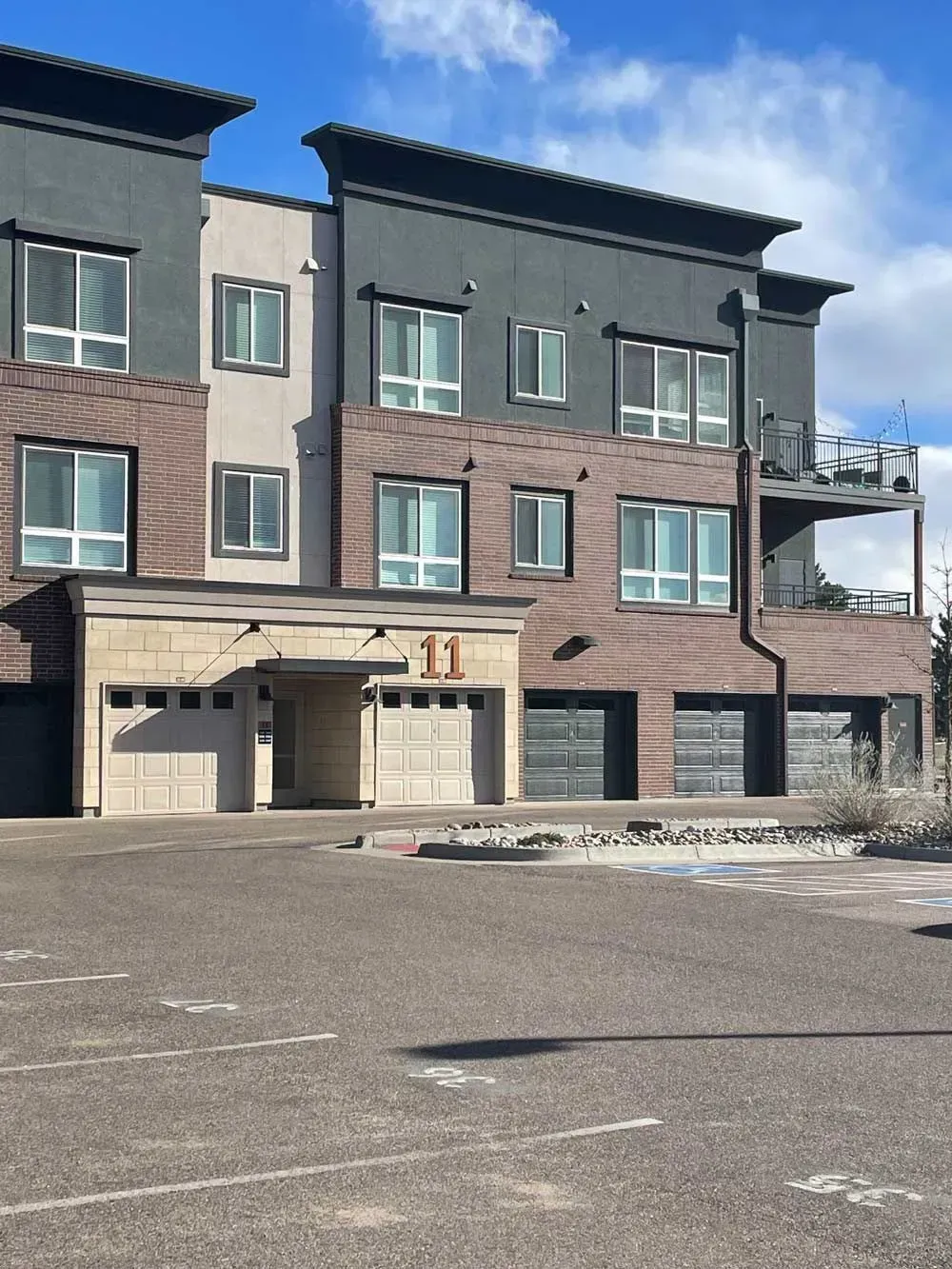Multi-story apartment building with brick and gray accents; garage doors below.