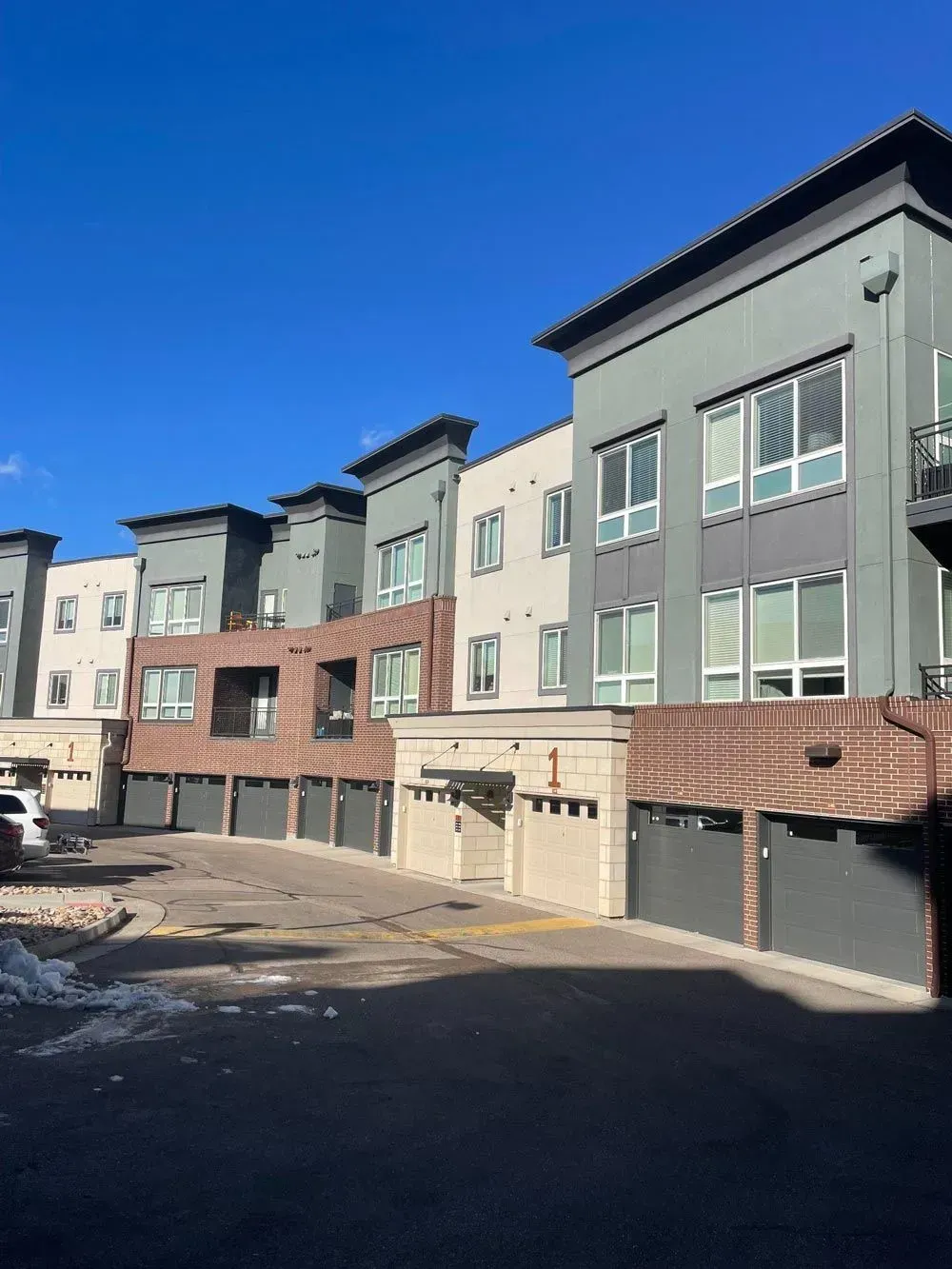 Multi-story townhomes, mostly gray and brick, with garage access and a clear blue sky.