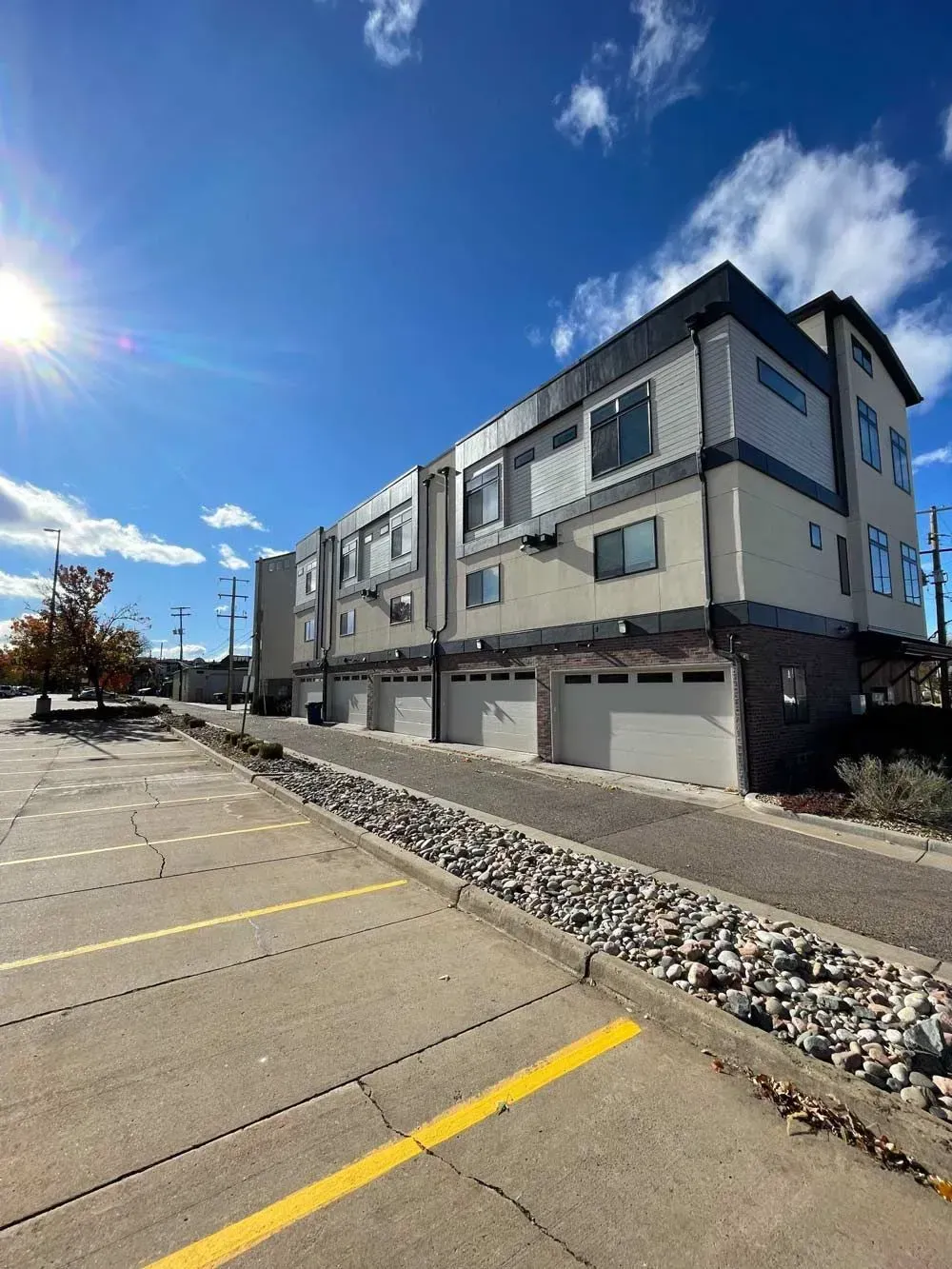 Multi-story modern townhouses with garages, parked cars, and a sunny sky.