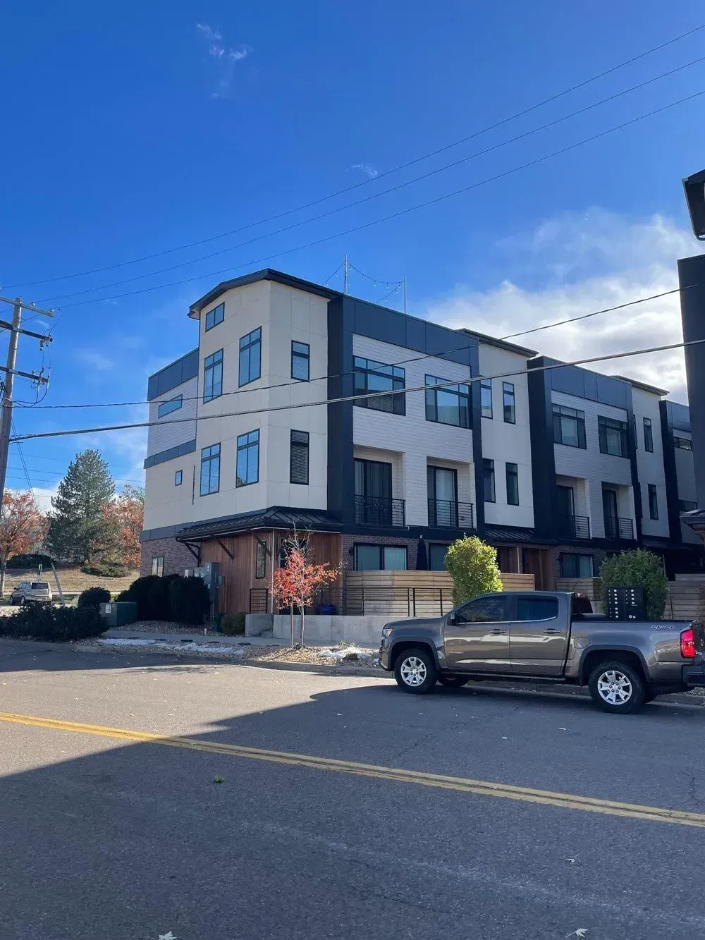Modern townhouses with light and dark contrasting walls, parked truck on the street under a clear blue sky.