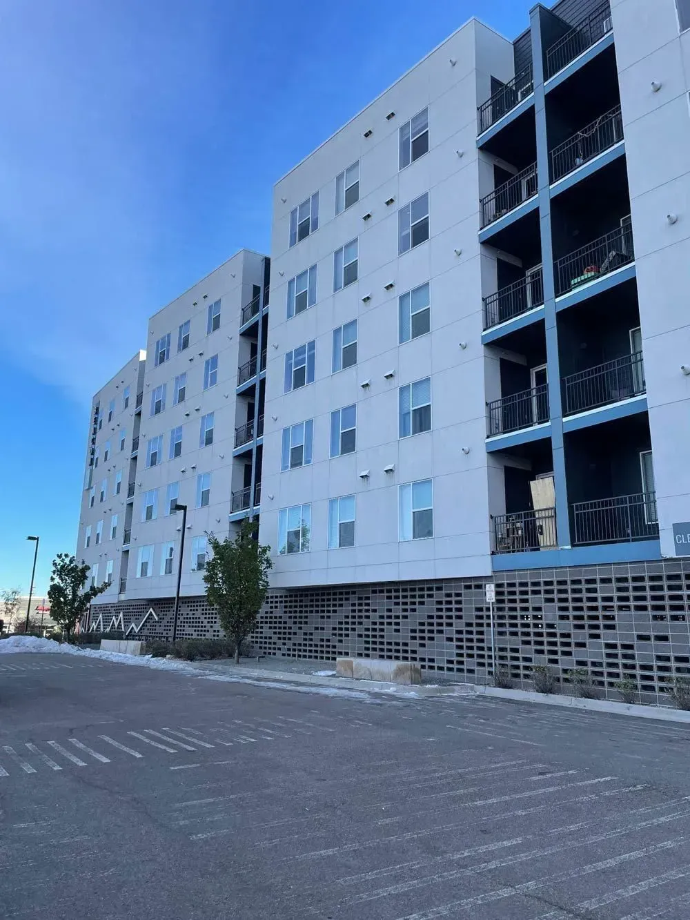 Multi-story apartment building with white siding, blue trim, and gray brickwork on a paved lot.