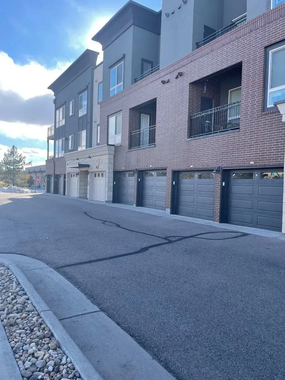 Building with garages, brick and gray facade, sidewalk, asphalt road, blue sky.
