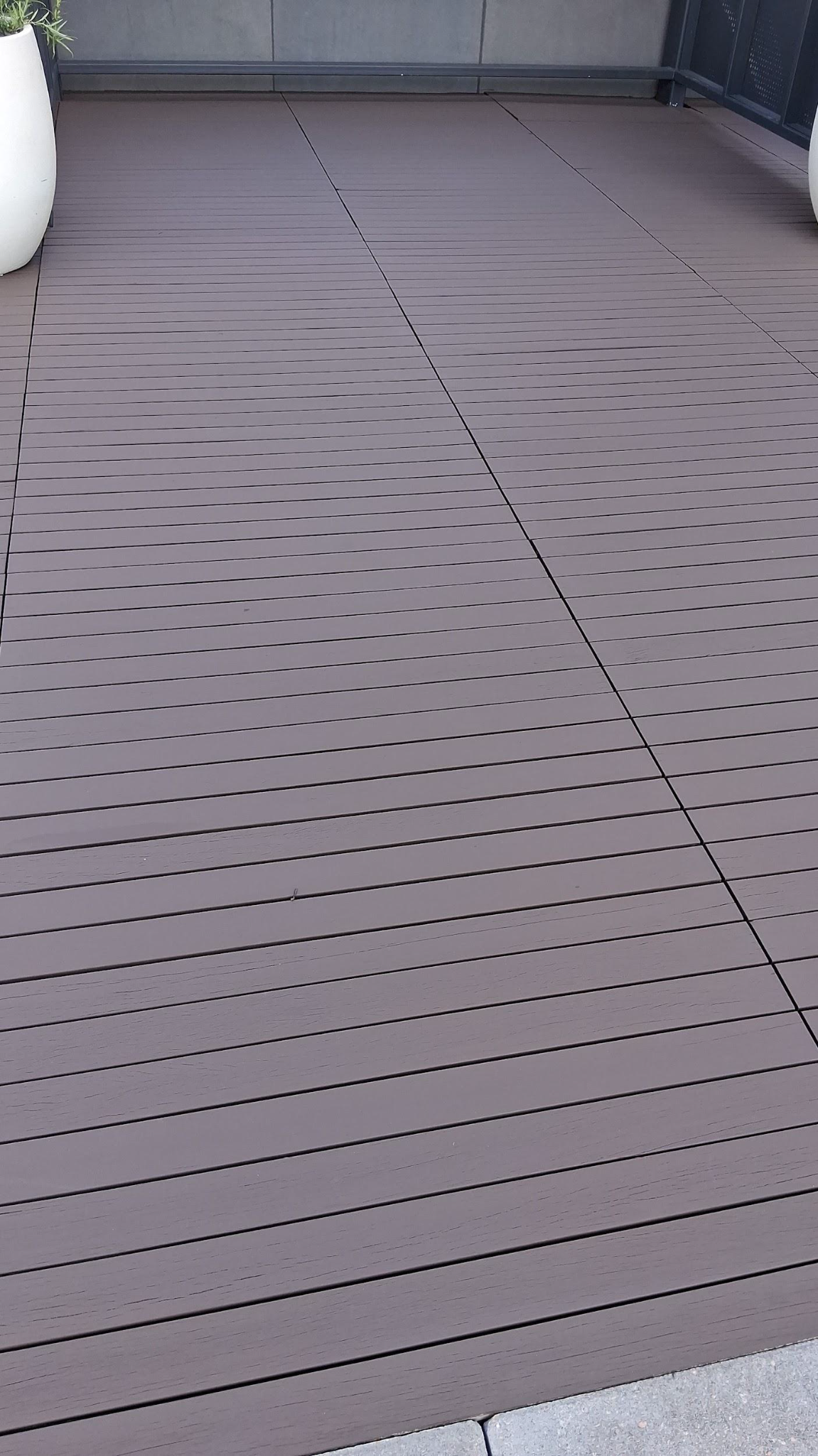 Gray perforated outdoor deck flooring with a diagonal seam line near a wall