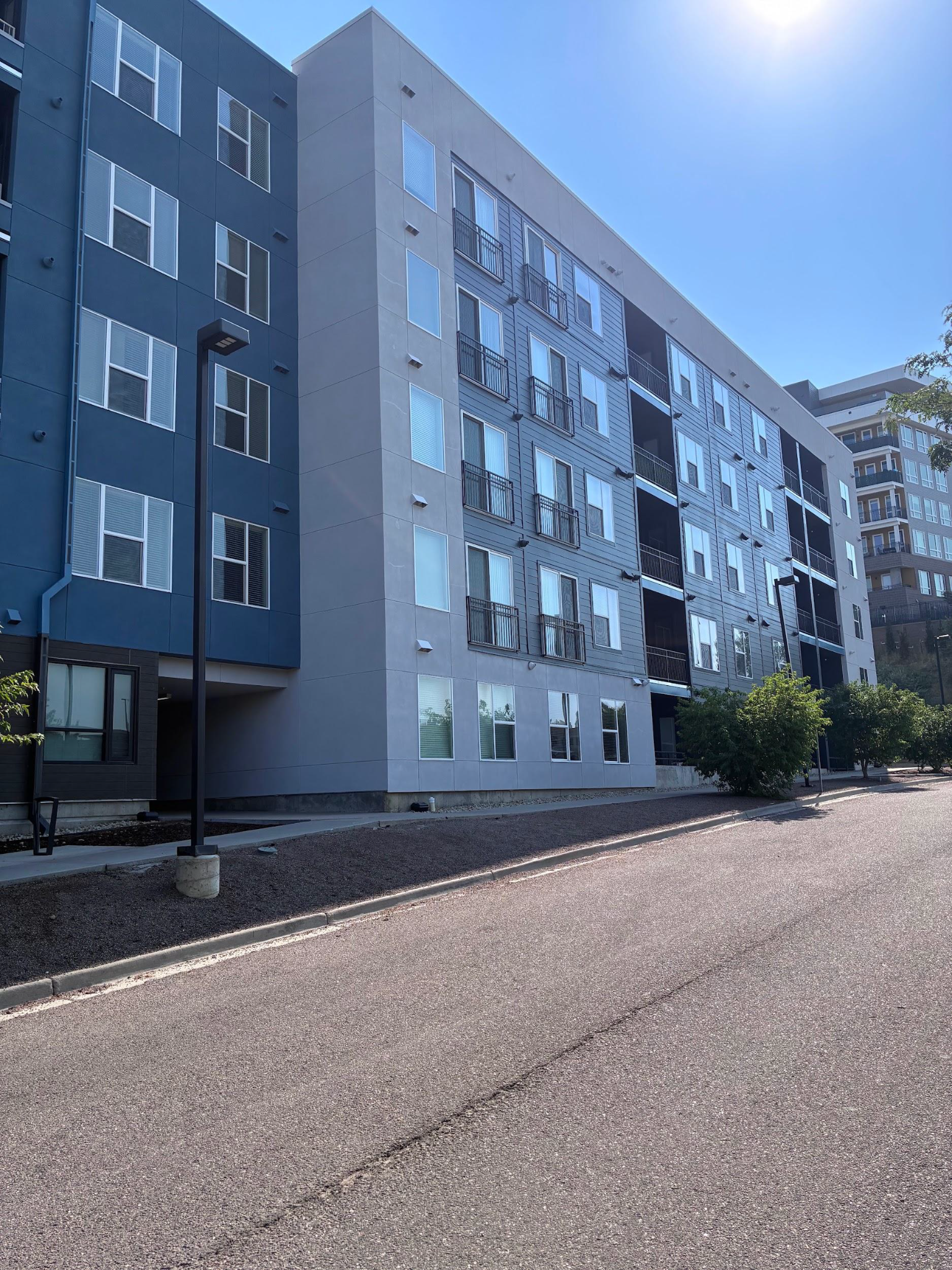 Modern apartment buildings along a gravel lot under a bright blue sky
