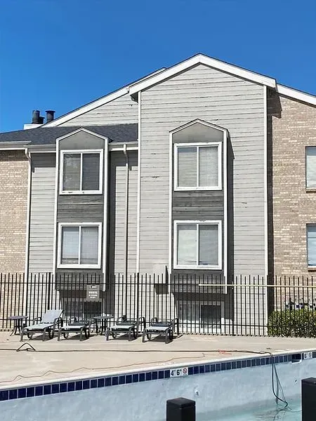 Apartment building exterior with pool; grey siding, brick, and fence; blue sky.