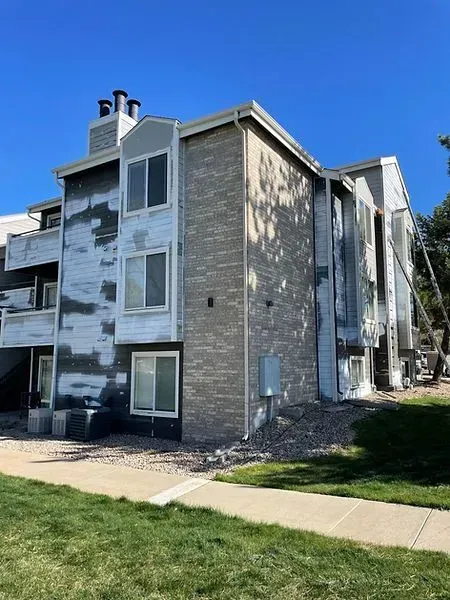 Apartment building with peeling paint, undergoing renovations. Brick and siding exterior, blue sky.