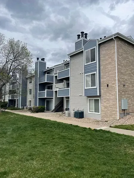 Apartment building with blue and gray siding, balconies, green lawn under cloudy sky.