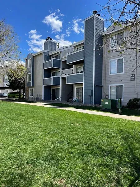 Apartment building with blue and gray siding, balconies, and green lawn on a sunny day.