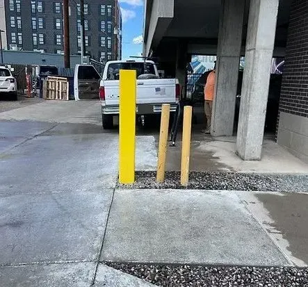 Yellow bollard and two wooden posts block a driveway. A truck is parked behind them.