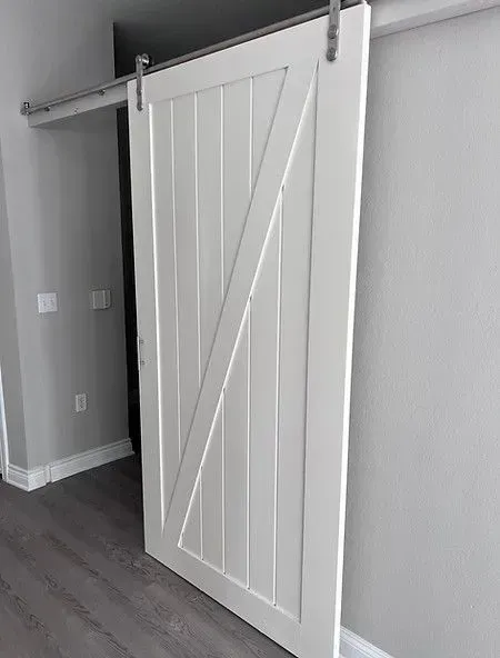 White barn door with diagonal brace, sliding on a metal track, mounted on a gray wall.