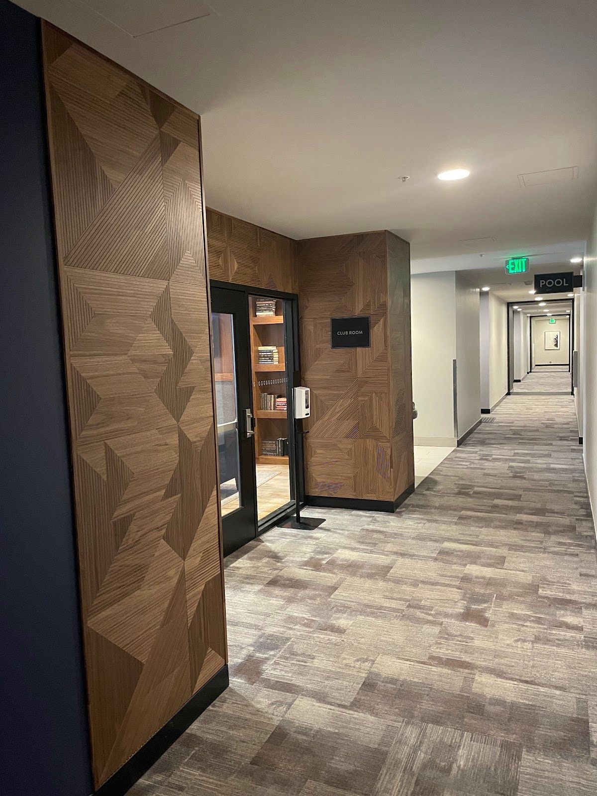 Hallway with patterned carpet, wood-paneled walls, and a room with a glass door.