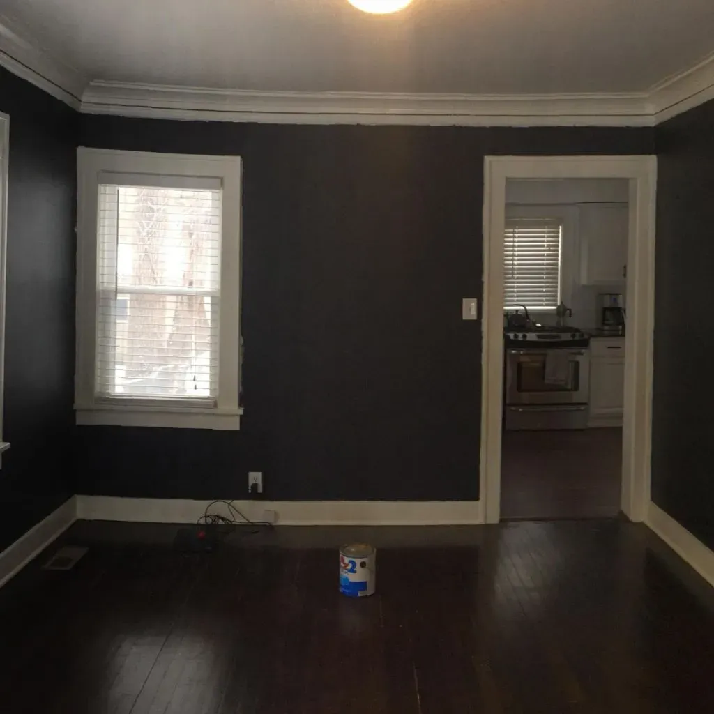 Dark-painted room with white trim, window, doorway, and can of paint on a dark wood floor.