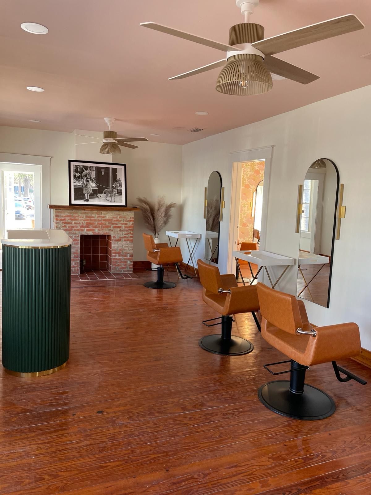 Hair salon interior with orange-toned floor, chairs, and pink ceiling. Mirrors, brick fireplace, and green column.