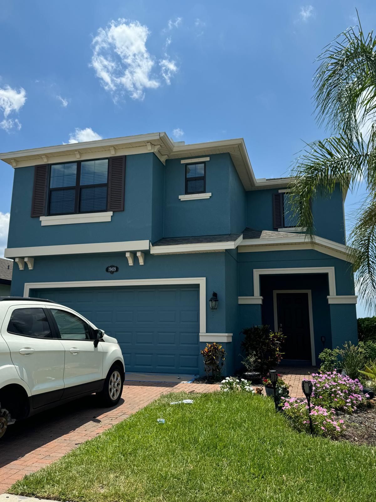Two-story teal house with a white SUV parked in the driveway. Green lawn and blue sky.