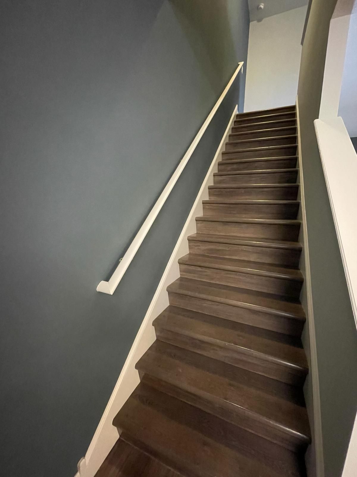 Staircase with brown wooden steps, white trim, and a blue-grey wall.