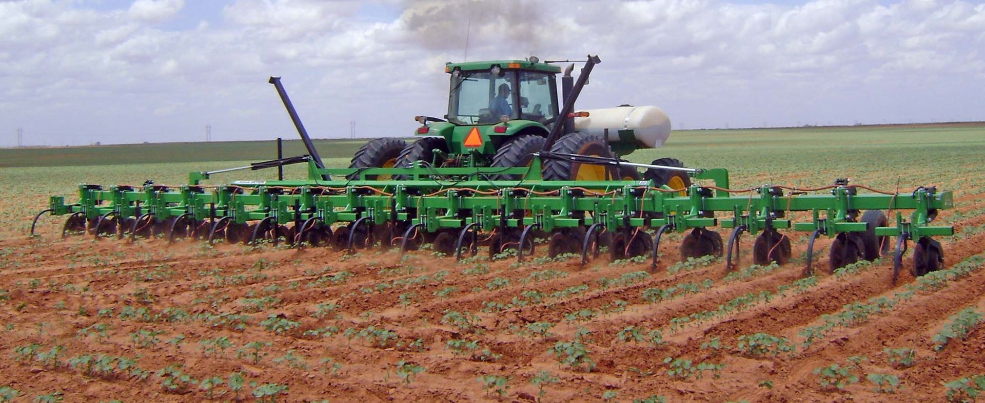 A green john deere tractor is plowing a field