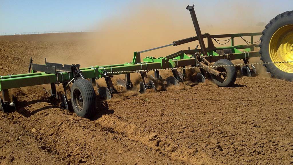 A green and yellow tractor is plowing a dirt field