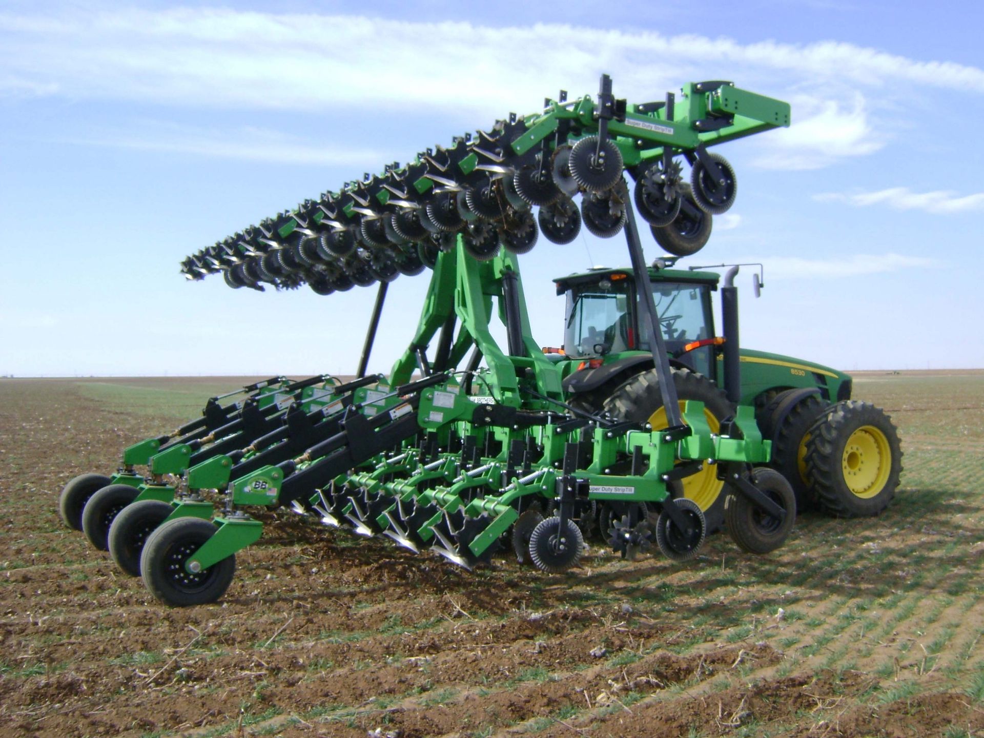 A green john deere tractor is plowing a field