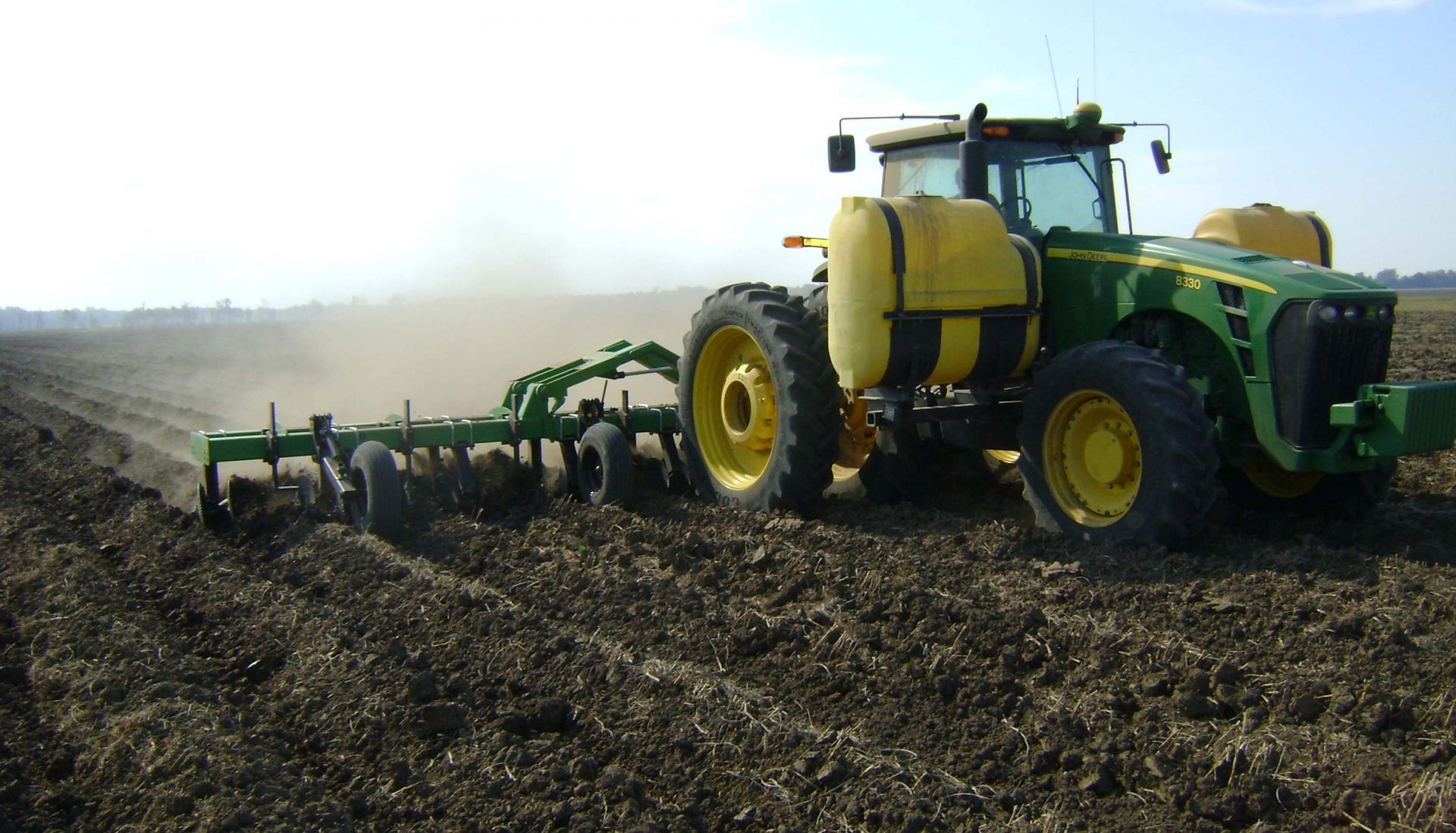 A green and yellow john deere tractor plowing a field