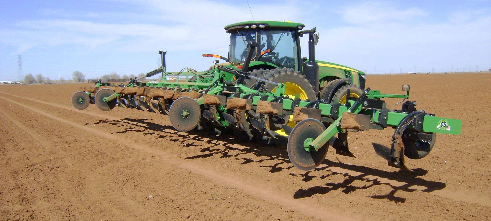 A green john deere tractor is plowing a dirt field