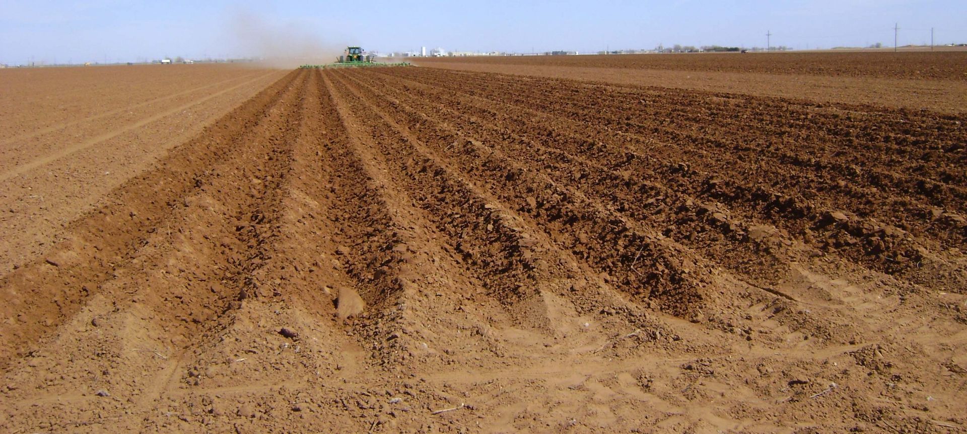 A tractor is plowing a field of dirt with a blue sky in the background.