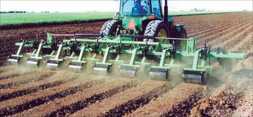 A green tractor is plowing a field with a plow attached to it.