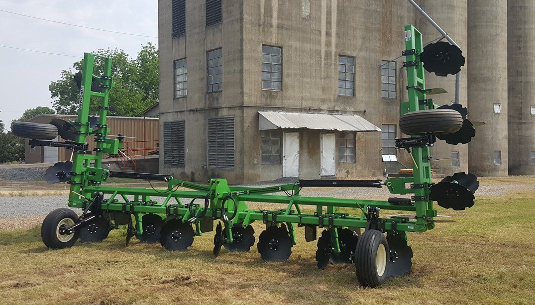 A green tractor is parked in a field in front of a building.
