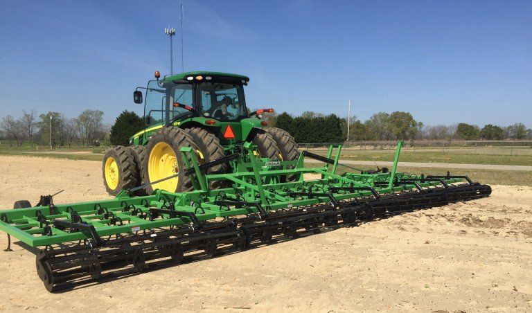 A green john deere tractor is parked in a dirt field.