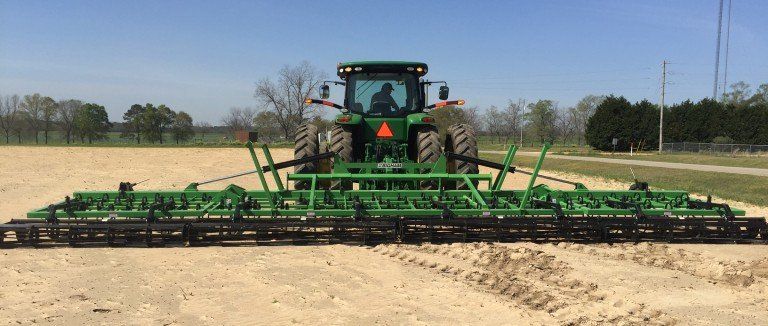 A green tractor is plowing a field on a sunny day.