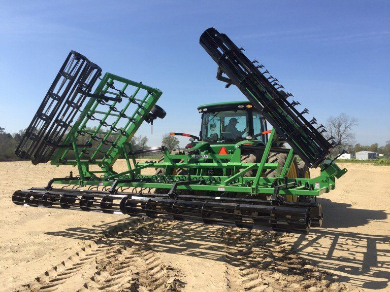 A green and black tractor is parked in a dirt field.