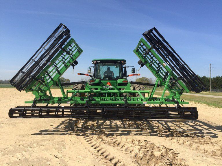 A green and black tractor is parked in a dirt field