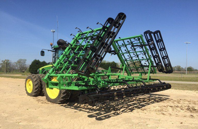 A green and black tractor is sitting on top of a dirt field.