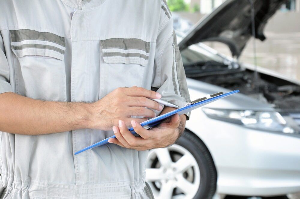 A Man is Holding a Clipboard in Front of a Car With the Hood Open — Bittkau Auto Care in Maroochydore, QLD