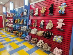 Stuffed bears and plush toys displayed on red wall shelves in a colorful store aisle.