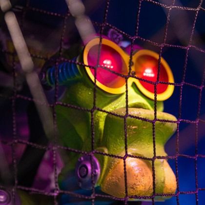 Colorful frog figurine behind a net, with glowing red eyes in dim purple light