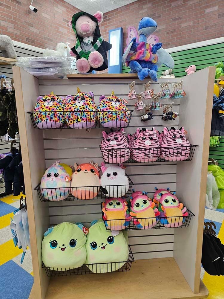 Shelf of colorful plush toys and keychains in a store display, including pink bags and pastel characters
