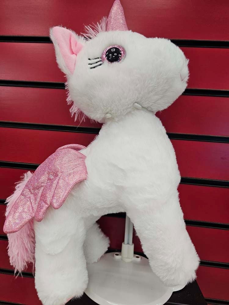 White plush unicorn with pink wings and mane on a stand against a red slat wall