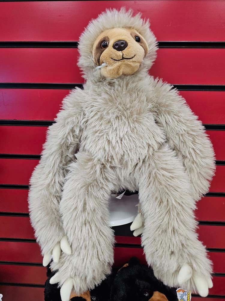 Fluffy beige stuffed sloth toy hanging against a bright pink slatted wall