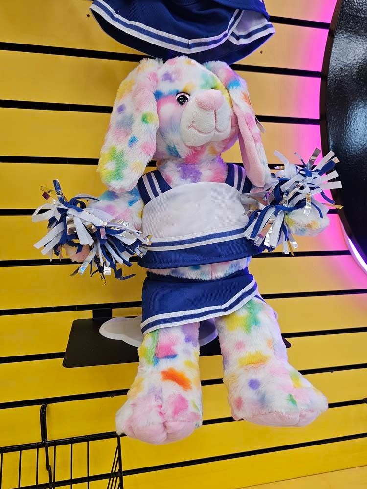 Pastel tie-dye plush bunny cheerleader on a store shelf with pom-poms and striped outfit