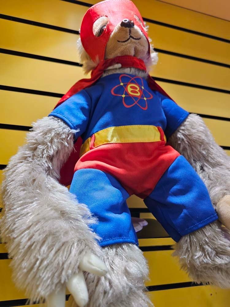 Red and blue plush doll with furry arms hanging against a yellow slat wall