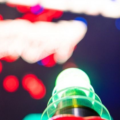 Glowing green lighthouse beacon against blurred red, white, and blue lights at night