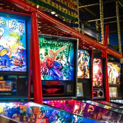 Row of colorful pinball machines in an arcade, including a Spider-Man game, under bright red framing.