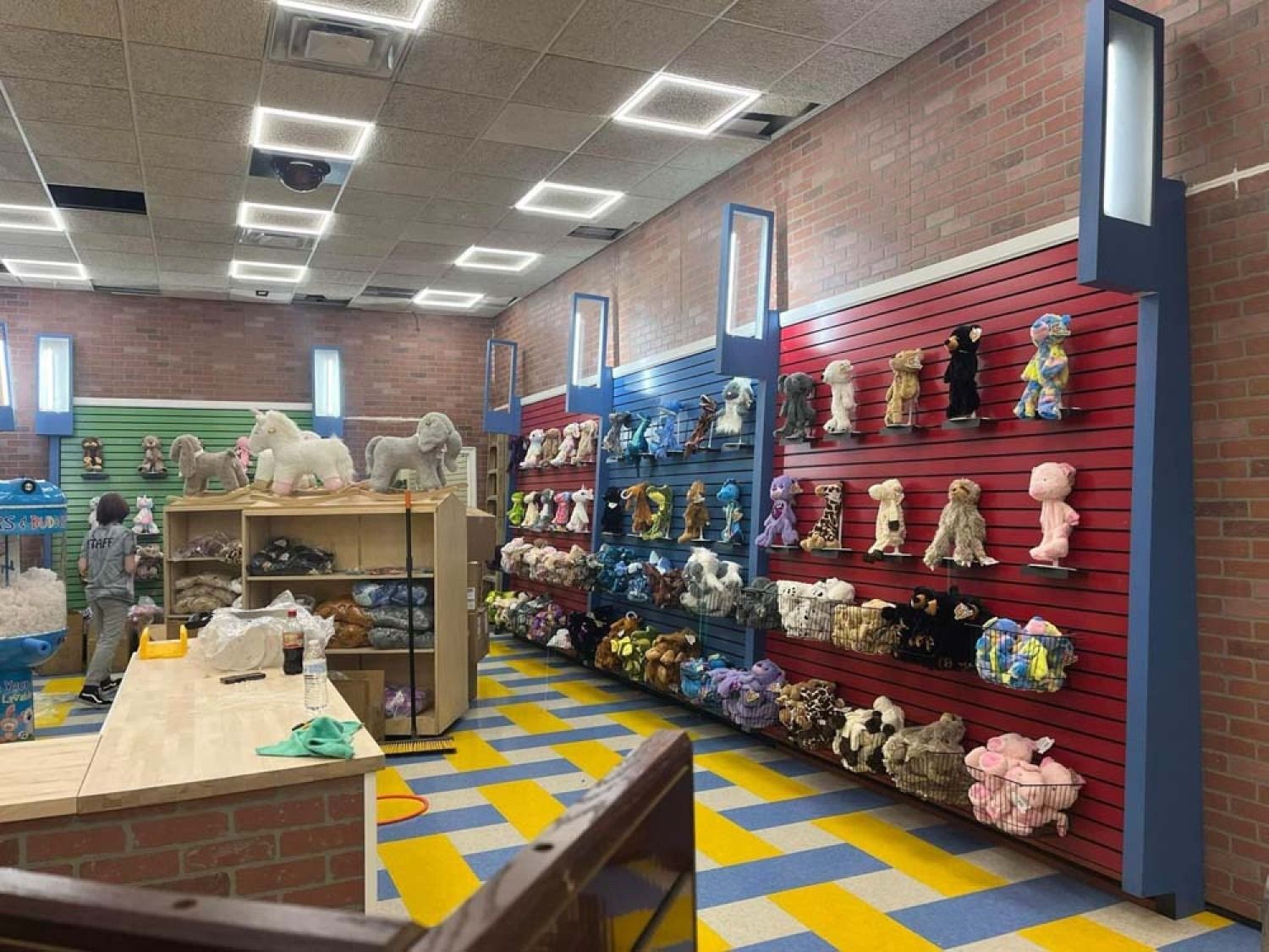 Colorful toy shop interior with stuffed animals on shelves, brick walls, and yellow-blue checkered floor