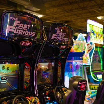 Row of Fast & Furious-themed arcade racing cabinets with neon-lit screens in an arcade hall