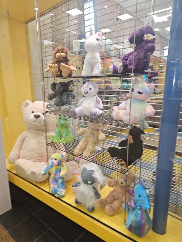 Stuffed animals displayed in a store claw machine, including teddy bears, a bunny, and colorful plush toys