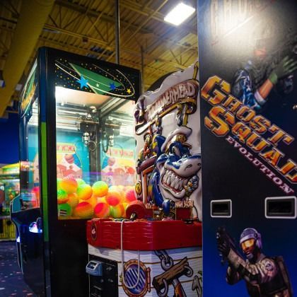 Arcade claw machine with glowing multicolored balls beside Ghost Squad arcade cabinet artwork