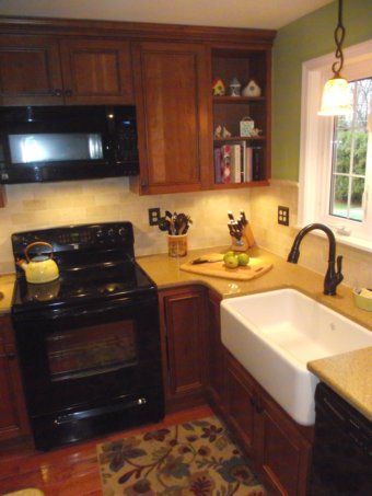 Cozy kitchen with black stove, wood cabinets, tan counters, and a white farmhouse sink by a window.