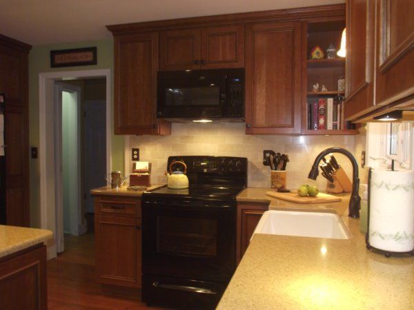 Kitchen with wooden cabinets, black stove, microwave, and white countertops under warm lighting