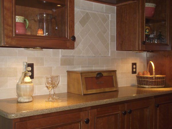 Kitchen counter with wooden cabinets, beige tile backsplash, and a basket of fruit near a lit candle
