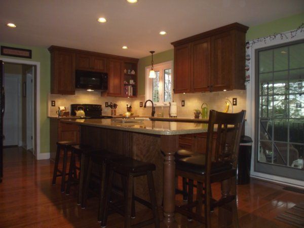 Warm kitchen with dark wood cabinets, center island, bar stools, and tiled floor beside a large window.